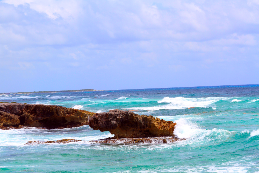 Ocean waves meeting rocky cliffs reflect the grounding and flow gained from practicing a list of somatic exercises, supporting balance, awareness, and emotional release. Waves crash against rocky cliffs under a bright sky, symbolizing strength, flow, and resilience—echoing the balance and awareness found in exploring a list of somatic exercises.