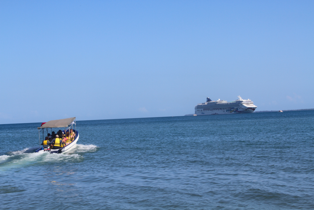 A boat gliding across open water toward a cruise ship reflects the steady rhythm and calming flow of somatic breathing activities that ease stress and restore balance. A small boat with passengers heads toward a distant cruise ship on calm blue water, symbolizing flow, rhythm, and presence found through somatic breathing activities.