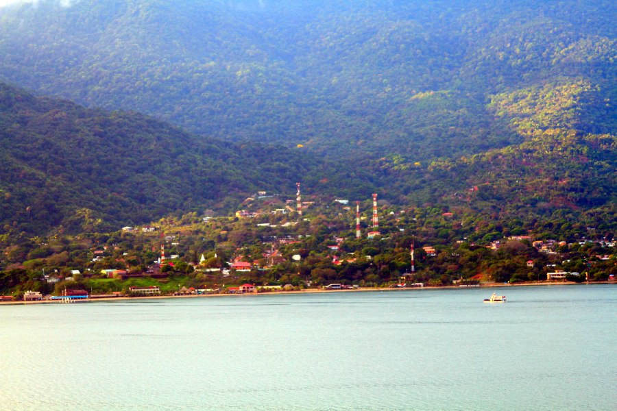 Scenic view of a town by the mountains and sea, representing the calming, restorative qualities of a somatic movement exercise for balance and connection. A small town at the base of lush green mountains beside calm waters, symbolizing grounding, balance, and the gentle practice of a somatic movement exercise in daily life.